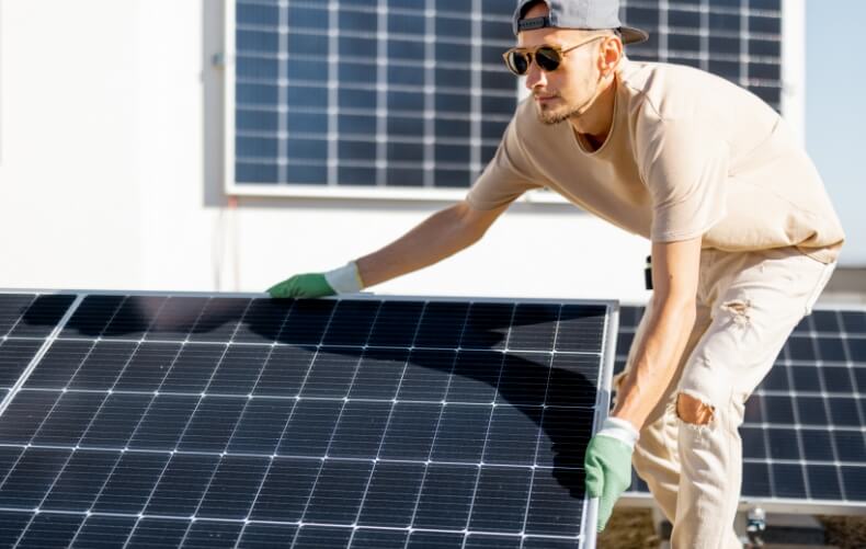 Ein junger Mann mit Sonnenbrille installiert ein Photovoltaik-Modul auf seiner Garage in einem DIY-Solar-Projekt